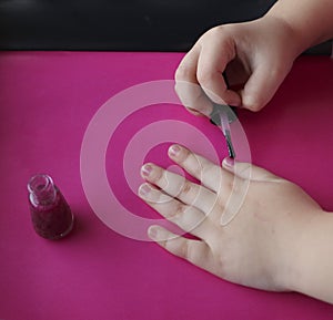 Children`s hands paint their nails with pink shiny nail polish.