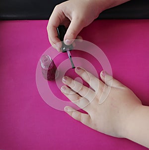 Children`s hands paint their nails with pink shiny nail polish.