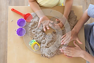 Children`s hands playing with kinetic sand and toys on the table.