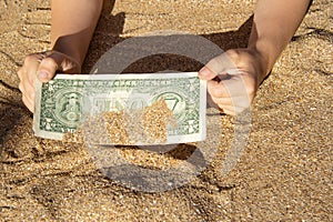 Children`s hands pull a bill of one dollar from the sea sand. A finding on vacation. Finance, sea, vacation