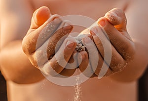 Children's hands release the falling sand. Sand flowing through your hands in the sunset sunlight