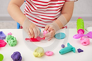 Children`s hands sculpt plasticine figures with rolling pin on white table, games with play dough, playdough, mass for modeling,