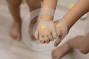 Children`s hands, sisters hold together. Gold tattoo on the arms, as a symbol of love, friendship.