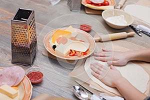 Children`s hands smoothen dough for pizza on a wooden table, children`s cooking lesson. photo