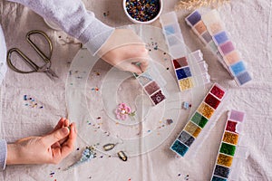 Children`s hands take a bead and boxes with beads for weaving a bracelet. Top view. Ð¡hildren`s hobby