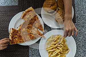 Children`s hands to take fast food on the table. Pizza, hamburger, fries