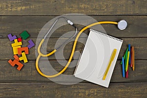 Children's healthy development concept - blank notepad, yellow stethoscope, colorful wooden jigsaw puzzles, crayons