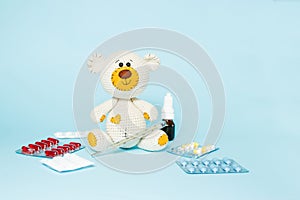 Children`s knitted toy teddy bear with pills takes the temperature of a mercury glass thermometer on blue background. Child`