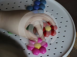 Children`s mosaic. the child lays a flower out of a colored plastic mosaic. the child`s hand holds a bright plastic mosaic piece