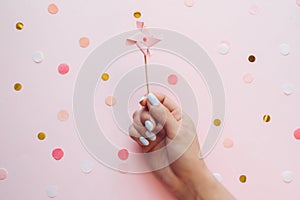 Children`s pastel weather vane topper for a cupcake in the hand of a girl with manicure on a pink background with confetti.