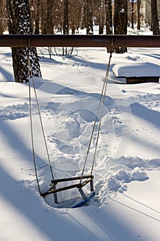 Children`s playground with swings covered with snow
