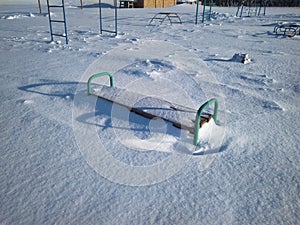 Children`s Playground with swings covered with snow in winter a bench in a snowdrift