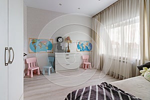 A children\'s room with a pink and blue chair, a window and a map on the wall