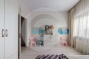 A children\'s room with a pink and blue chair, a window and a map on the wall