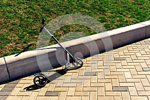 Children's scooter parked near the concrete curb. Outdoor Fun in the Summer