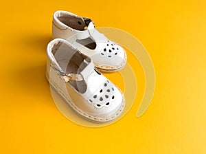 Children`s shoes, the concept of the first step. Baby white on a yellew background. Space for the text. The first steps of t