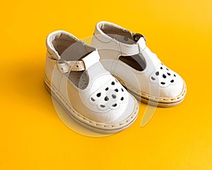 Children`s shoes, the concept of the first step. Baby white on a yellew background. Space for the text. The first steps of t