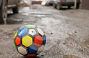 Children`s soccer ball game is on a dirty broken street road among puddles and residential yards of houses