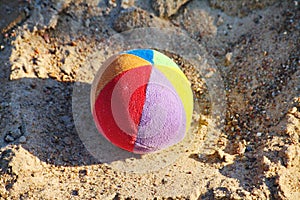 Children's soft fabric and striped multi-colored ball about the yellow quartz sand of the bright sun.