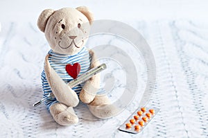 Children's soft toy teddy bear with pills takes the temperature of a mercury glass thermometer. child' disease.