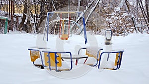 Children's swing swinging from the wind in winter, children's playground in the snow