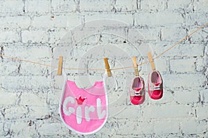 Children`s toddler pink saliva and red shoes on a rope against a white brick wall.