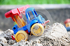 Children s toy car, colorful plastic lorry on sand. Close-up. Selective focus. Copy space