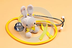 Children`s toy with a Childhood Cancer Awareness Golden Ribbon and stethoscope on yellow background