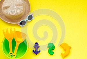 Children`s toys for sand on yellow background with a hat and glasses, space for copy space.