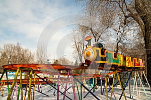 A children`s train rides on high rails over snowdrifts among trees in a city amusement park