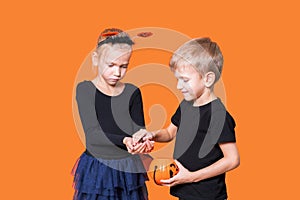 Children's trick or treat is a Halloween tradition. Boy and girl holding an orange pumpkin-shaped basket with treats