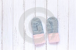 Children`s winter accessories, warm knitted mittens - gray with pink hearts on white wooden background.