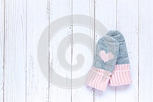 Children`s winter accessories, warm knitted mittens - gray with pink hearts on white wooden background. Flat lay, copy
