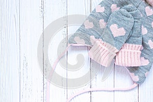 Children`s winter accessories, warm knitted mittens and hat - gray with pink hearts on white wooden background.
