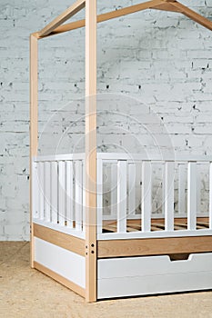 Children's wooden bed in the form of a house on a background of a brick wall.