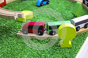 Children`s wooden train with cars, railway and wooden trees on artificial plastic green grass. Early childhood education,