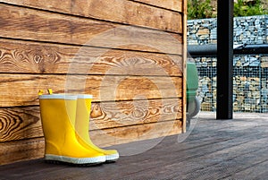 Children`s yellow rubber boots stand on the terrace of a wooden house