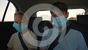 Children in safety mask in car go to school. Two children in the back seat of car are traveling with their family. Happy