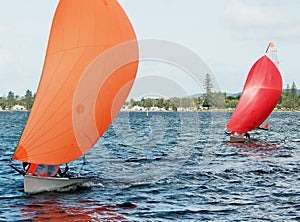 Children Sailing small sailboat with colourful orange and red sails on an inland lake