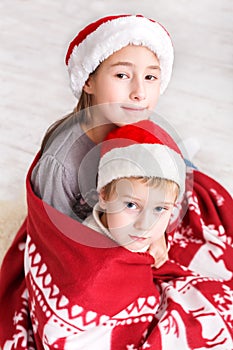 Children in santa hats near christmas tree, wait for holidays
