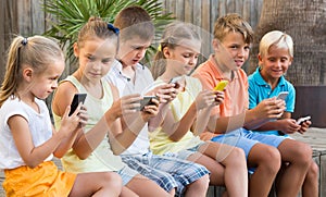 children in school age looking at mobile phones and sitting outdoors