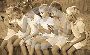 children in school age looking at mobile phones and sitting outdoors