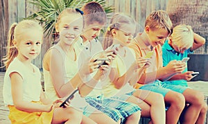 children in school age looking at mobile phones and sitting outdoors