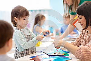 Children with scissors in hands cutting paper with teachers in class room. Group of children doing project in