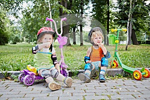 Children scooterists rest sitting on curb of