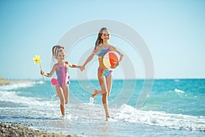 Children at sea play merrily. Two sisters run, jump on the beach in summer.