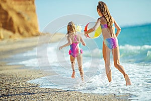 Children at sea play merrily. Two sisters run, jump on the beach in summer.