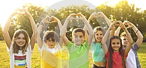 Group of joyful preteen kids standing in sunny park with arms raised show heart shape made by hands