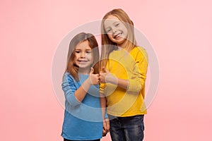 Children showing like, approval sign. Two adorable happy little girls gesturing thumbs up together and smiling to camera