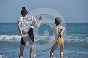 Children, siblings playing on the sea shore. They jumping in the waves